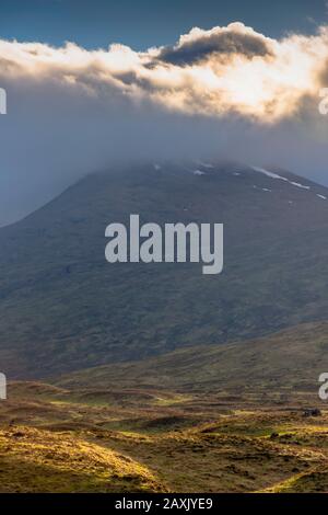 Extreme Wetterbedingungen in den schottischen Highlands. Niedrige Wolken, die von oben durch die Sonne erhellt werden und Berggipfel mit Resten von Schnee und Flecken von s bedecken Stockfoto