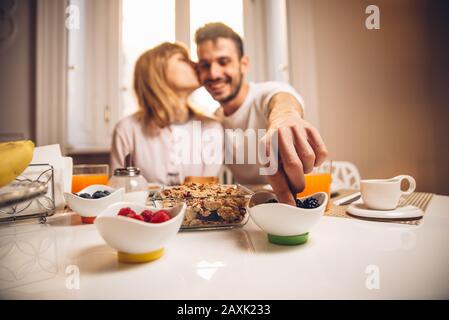 Junges glückliches Paar, das am Tisch sitzt und morgens zusammen frühstücken kann. Konzentrieren Sie sich auf die Hand. Stockfoto