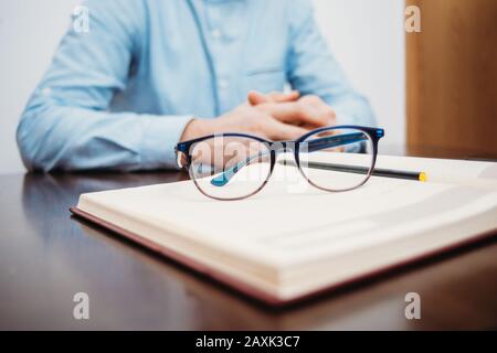 Brille auf Buch mit den Händen des Mannes im Büro Stockfoto