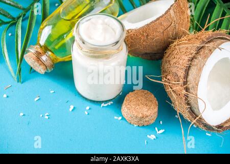 Kokosöl im Glasbecher mit tropischen Blättern und frischer Kokosnuss. Konzept für organische mct-Öle. Türkis, Aquamarin Hintergrund Stockfoto
