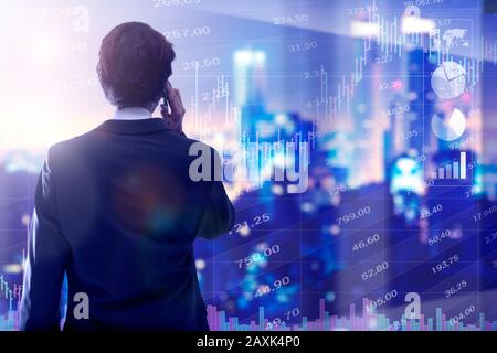 Geschäftsmann auf seinem Rücken telefoniert. Im Hintergrund die Stadt in der Nacht mit Börsenchart und vielen Schaubildern. Finanzen und Kommunikation Stockfoto