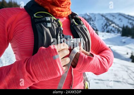 Junge Frau schneit den Rucksack, bevor sie im Winter joggt, auf dem Schnee auf dem Bergpfad Stockfoto