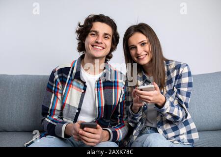 Glückliches Paar, das im Wohnzimmer Smartphones mit einem Lächeln verwendet. Stockfoto