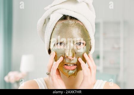 Porträt Der Schönen Jungen Frau in weißem Handtuch auf dem Kopf Mit kosmetischem Blatt Goldmaske Auf dem Gesicht der Schönheit. Hautpflegekonzept Stockfoto