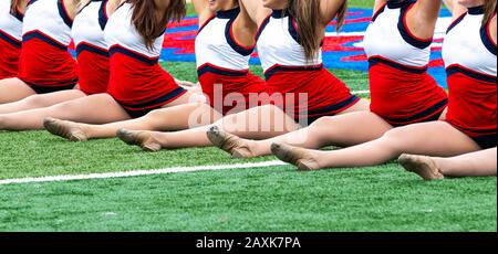 Ein Kickline-Team von High-School-Mädchen steht in einer kompletten Frontpartie auf einem grünen Rasenplatz. Stockfoto