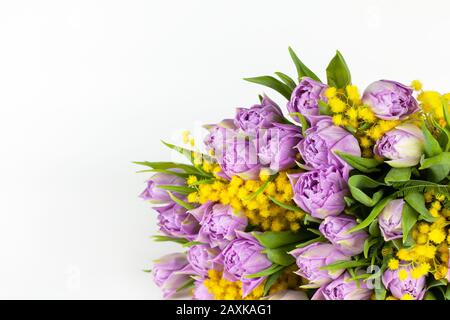 Blumenstrauß aus lila Tulpen und gelben Mimosen auf weißem Hintergrund, Kopierraum, Seitenansicht, Nahaufnahme. März, 14. Februar, Geburtstag, Valentinstag, Mutter, Stockfoto