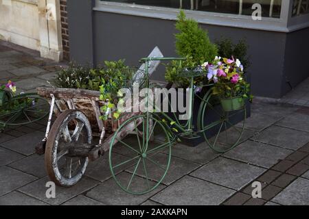 Interessante Blumendarstellung in alten Holz-Schubkarren- und Fahrradrahmen in Der High Street, Esher, Surrey, Großbritannien Stockfoto