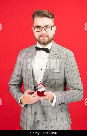 Vorderansicht des Mannes im Anzug, der den Eingriffsring isoliert auf rotem Hintergrund hält. Stockfoto