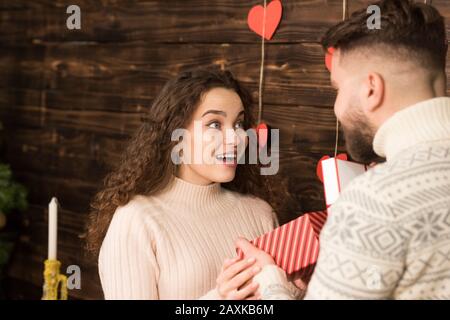 Teilweiser Blick auf den Mann, der am valentinstag der schockierten Freundin ein Geschenk überreicht. Stockfoto