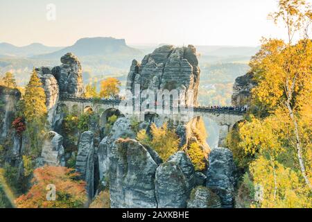 Historische Bastei-Brücke in der Sächsischen Schweiz im Herbst. Felsen und Bäume mit blauem Himmel und Sonnenschein. Elbtal mit Bergen im Hintergrund Stockfoto