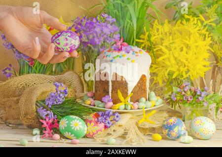 Ostereier und Osterdekoration auf dem Holzhintergrund. Hände halten gemaltes Osterei. Bunte ostereier in weiblicher Hand. Stockfoto