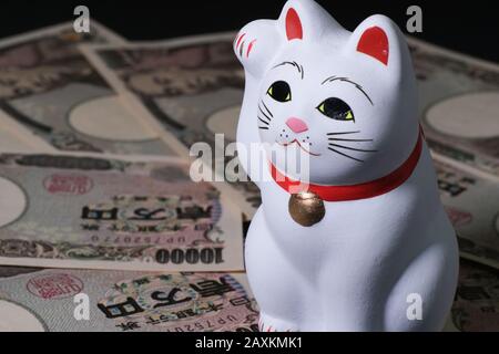 Nahaufnahme einer japanischen Glückskatze (Maneki-neko) auf Japanisch 10000 Banknoten Stockfoto