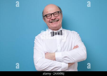 Glücklicher ranghoher hispanischer Kahlmann in einer Brille, der mit gefalteten Händen auf der Kamera lächelt. Studio gedreht Stockfoto
