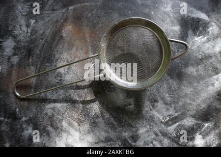 Feinmasch-Sieb aus Edelstahl, Kälte Mehlsieb mit Griff auf dunklem Hintergrund, mit Mehl bestäuben. Stockfoto