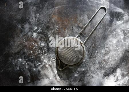 Feinmasch-Sieb aus Edelstahl, Kälte Mehlsieb mit Griff auf dunklem Hintergrund, mit Mehl bestäuben. Stockfoto