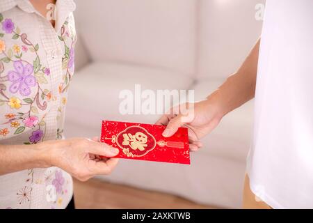 Übersetzungstext auf rotem Umschlag im Bild: Wohlstand und Frühling.Menschen Eltern geben roten Umschlag für chinesische Neujahrsfeiern oder Lunar-Neujahrsfeiern