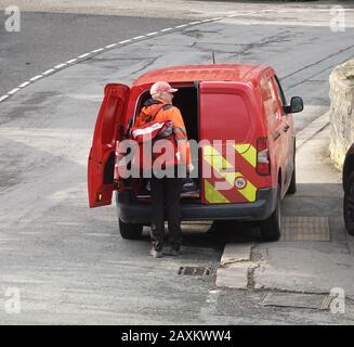 Ein Postbote holt seine Lieferungen vor seiner endgültigen Auslieferung des Tages von der Rückseite seines Transporters ab. Stockfoto