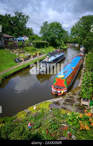 Blick von einer Brücke über den Kanal auf ein Boot, das mit vermoorten Schmalbooten beim Gnosall Canal Festival im Dorf Staffordshire UK vorbeifährt. Stockfoto