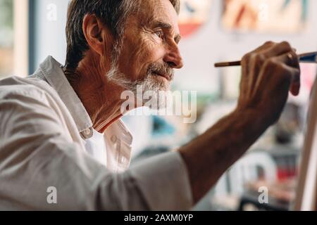 Nahaufnahme des Porträts des älteren Malers, der im Atelier auf Leinwand zeichnet Stockfoto