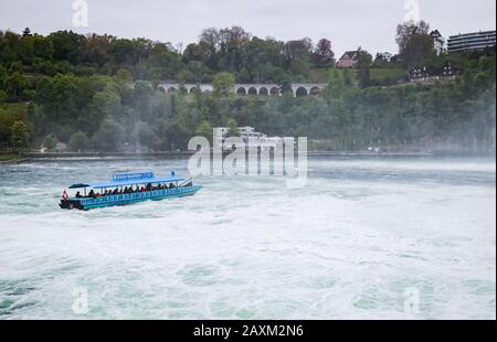 Rheinfall, Schweiz - 6. Mai 2017: Bootsfahrt zu den Rheinfällen, Touristen sind in blauem Motorboot auf unruhigen Gewässern Stockfoto