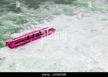 Rheinfall, Schweiz - 6. Mai 2017: Bootsfahrt zu den Rheinfällen, Touristen sind in rosafarbenem Motorboot auf unruhigen Gewässern Stockfoto