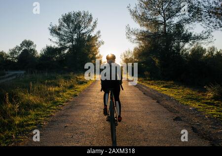 Radfahrerinnen, die in wenig Sonnenlicht fahren, umgeben von grünem, üppigem Wald mit Sonnenstern Stockfoto