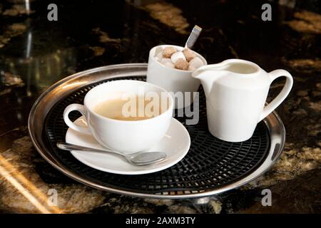Eine Tasse Kaffee mit Milchkanne und Zucker auf einem Tablett auf einer Marmorunterseite. Stockfoto