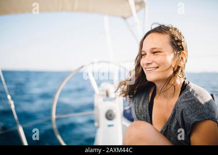 Junge Frau sitzt auf segelboot und lächelt glücklich Stockfoto