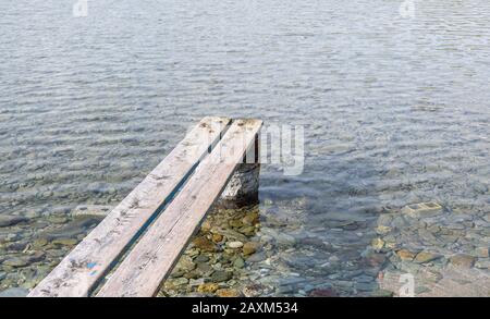 Verwitterter kleiner Steg aus Holz. Holzbohlen werden richtig auf rostigen Fass gestellt, um eine Mini-Plattform über einem transparenten, ruhigen blauen Meeresgrund zu schaffen. Stockfoto