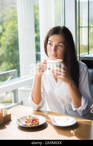 Schönen lächelnden jungen Frau im Cafe in der Nähe der Fenster mit Kaffee und leckeren Kuchen. Stockfoto