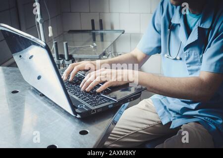Arzt in blauer Uniform sitzt am Tisch und tippt auf Laptop, Filter Stockfoto