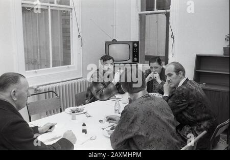 1960er Jahre, historische, männliche Krankenhauspatienten in Bademänteln saßen auf einem Tisch und frühstückten zusammen in einem gemeinsamen Speisesaal im Brook General Hospital, South London, England, Großbritannien. In der Ecke des Zimmers befindet sich ein Fernseher aus dieser Zeit mit Antenne. Stockfoto