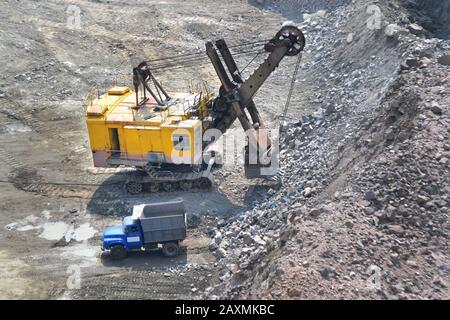 Riesiger gelber Bagger und ein blauer Lastwagen auf einem Steinbruch aus Granit, Filter Stockfoto