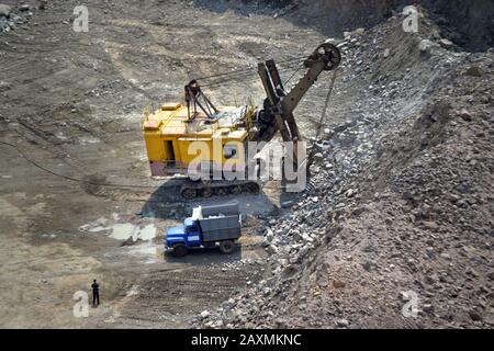 Riesiger Bagger, LKW und Mann stehen neben auf einem Steinbruch aus Granit Stockfoto