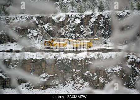 Gelbe Bergbaumaschinen an den hängen eines Granit-Steinbruchs im verschneiten Wintertag Stockfoto