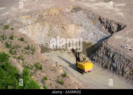 Der gelbe Baggerschnitzer steht vor Granitsteinen im Steinbruch für Granit auf dem Boden Stockfoto