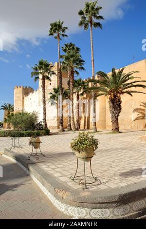 Die beeindruckenden Stadtmauern der Medina, umgeben von bunten Palmen und einem großen gepflasterten Gehweg in Sfax, Tunesien Stockfoto