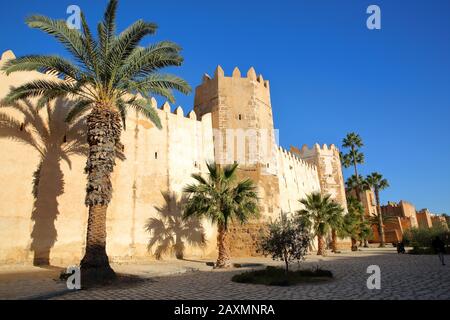 Die beeindruckenden Stadtmauern der Medina, umgeben von bunten Palmen und einem großen gepflasterten Gehweg in Sfax, Tunesien Stockfoto