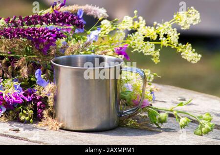 Wanderstahlbecher steht auf einem grauen Holztisch in der Nähe der Blumen Stockfoto