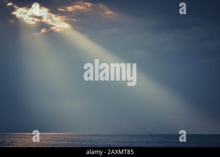 Die Strahlen der Sonne leuchten auf der Wasseroberfläche gegen den dunklen Himmel Stockfoto