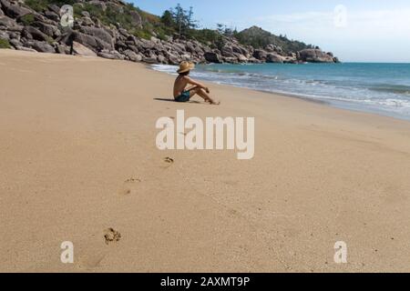 Fußabdrücke auf Sand, die von einem männlichen Touristen mit Hut und grünen Shorts hinterlassen wurden Stockfoto