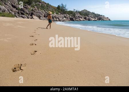 Fußabdrücke auf Sand, die von einem männlichen Touristen mit Hut und grünen Shorts hinterlassen wurden Stockfoto