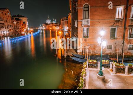 Venedig, Italien Nachtszenerie des Canal Grande, von Laternen beleuchtet und auf der Wasseroberfläche reflektiert. Majestätische Basilika Santa Maria della Salute im Hintergrund Stockfoto