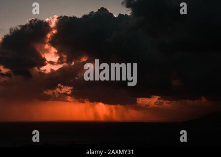 Sonnenuntergang an der Küste mit Regen am Horizont zwischen Wolken Stockfoto