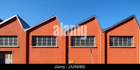 Altertümlicher Werkshall mit einer tief orangefarbenen Fassade an blauem Himmel, Zick-Zack-Dach und Fenstern in den südlichen Vorstädten Mailands, Italien Stockfoto