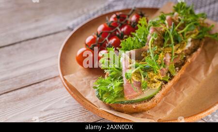 Nahaufnahme von Bruschetta mit rauchtem Fleisch, Frischkäse, Erbsenmikrogreen und Pesto, Kirschtomaten auf einem Holztisch Stockfoto