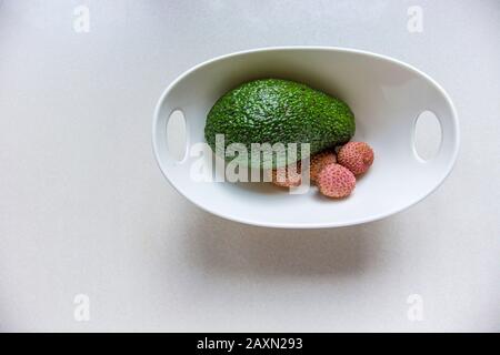 Grüner Avocado und Lychee in einer weißen Schüssel auf weißem Hintergrund, Draufsicht Stockfoto