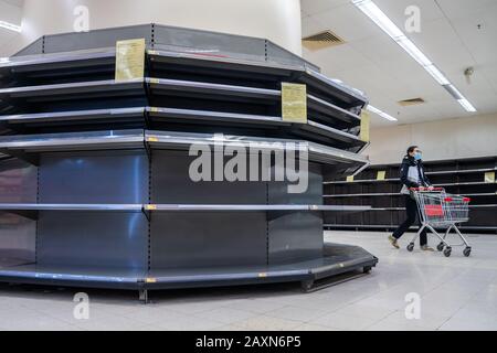 Ein weiblicher Shopper, der eine chirurgische Maske trägt, läuft an leeren Supermarktregalen vorbei, die normalerweise mit toilettenpapier und Küchenrollen bestückt sind.Panik wächst in Hongkong, da die Stadt den 50. Fall des Neuartigen Coronavirus (2019-nCoV) bestätigt hat. Mehr als 40.000 Fälle des Virus haben sich weltweit bestätigt, es hat bisher mehr als 1000 Leben gefordert. Stockfoto