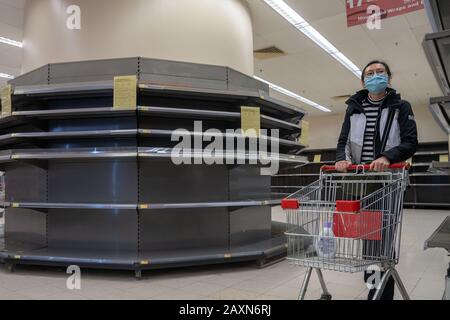 Ein weiblicher Shopper, der eine chirurgische Maske trägt, läuft an leeren Supermarktregalen vorbei, die normalerweise mit toilettenpapier und Küchenrollen bestückt sind.Panik wächst in Hongkong, da die Stadt den 50. Fall des Neuartigen Coronavirus (2019-nCoV) bestätigt hat. Mehr als 40.000 Fälle des Virus haben sich weltweit bestätigt, es hat bisher mehr als 1000 Leben gefordert. Stockfoto