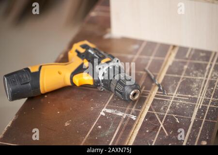 Bohrer mit Holzbrett in der Werkstatt, Nahaufnahme, verschwommener Hintergrund Stockfoto